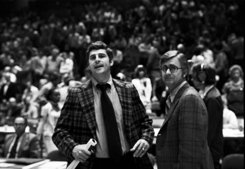 a black and white photo of IU basketball coach Bob Knight wearing a plaid jacket and a black tie, standing beside an unnamed man