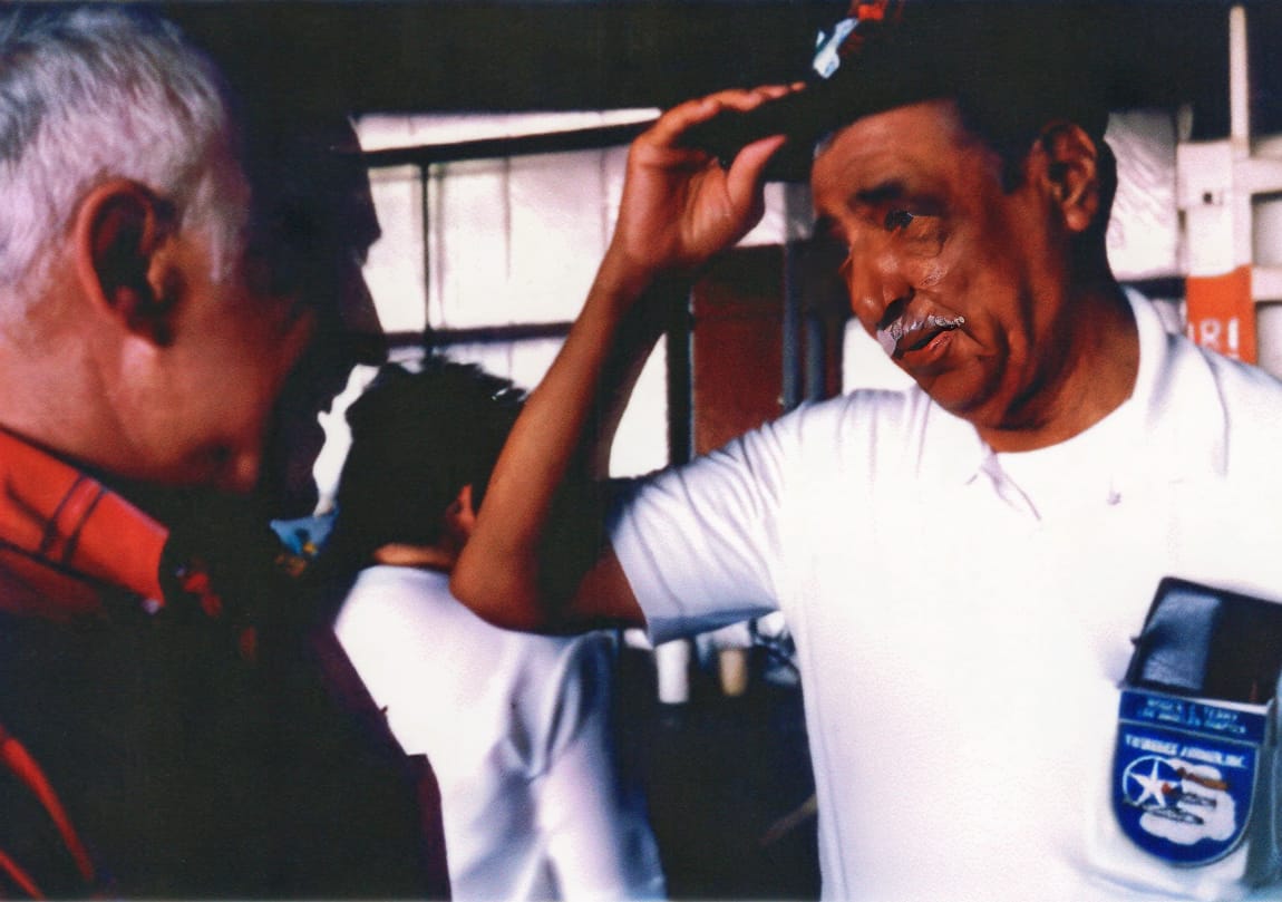 Jim Allsion, wearing the same red plaid shirt, speaks to Bill Terry, an elderly Black man, who is wearing a white shirt and a black cap