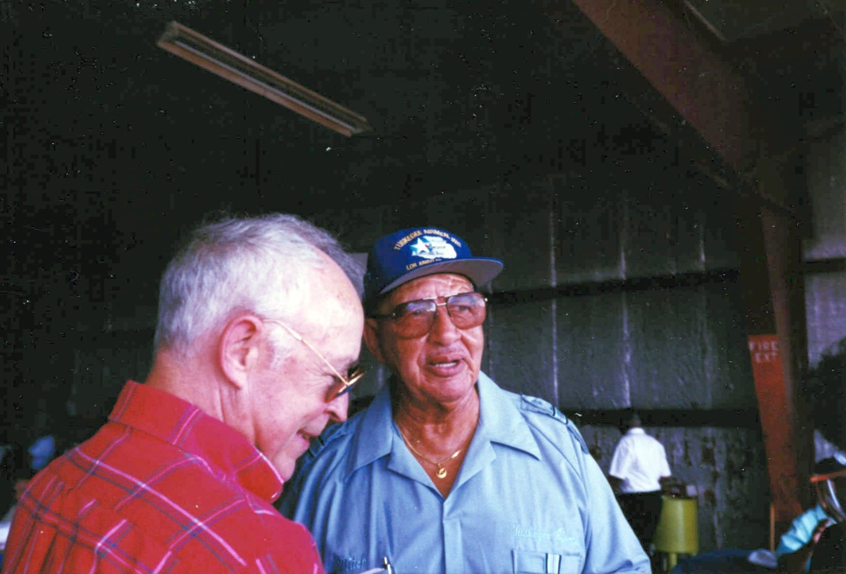 the author, Jim Allison, in a red plaid shirt. Air Force Lt. Col. James C. Warren stands beside him, looking into the distance, and wearing a blue hat, dark glasses, a gold necklace, and a blue shirt