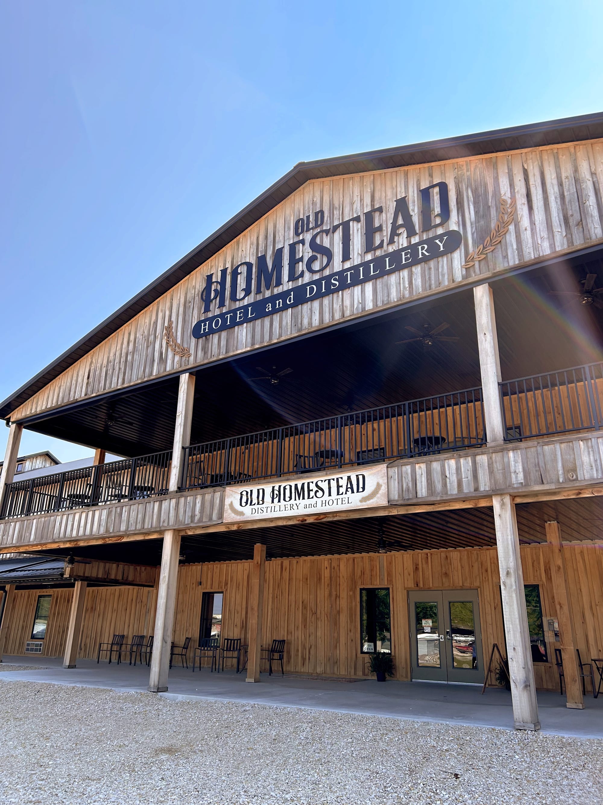 a wooden two-story structure with broad porches on the ground level and second floor. Large signs read "Old Homestead Hotel and Distillery"