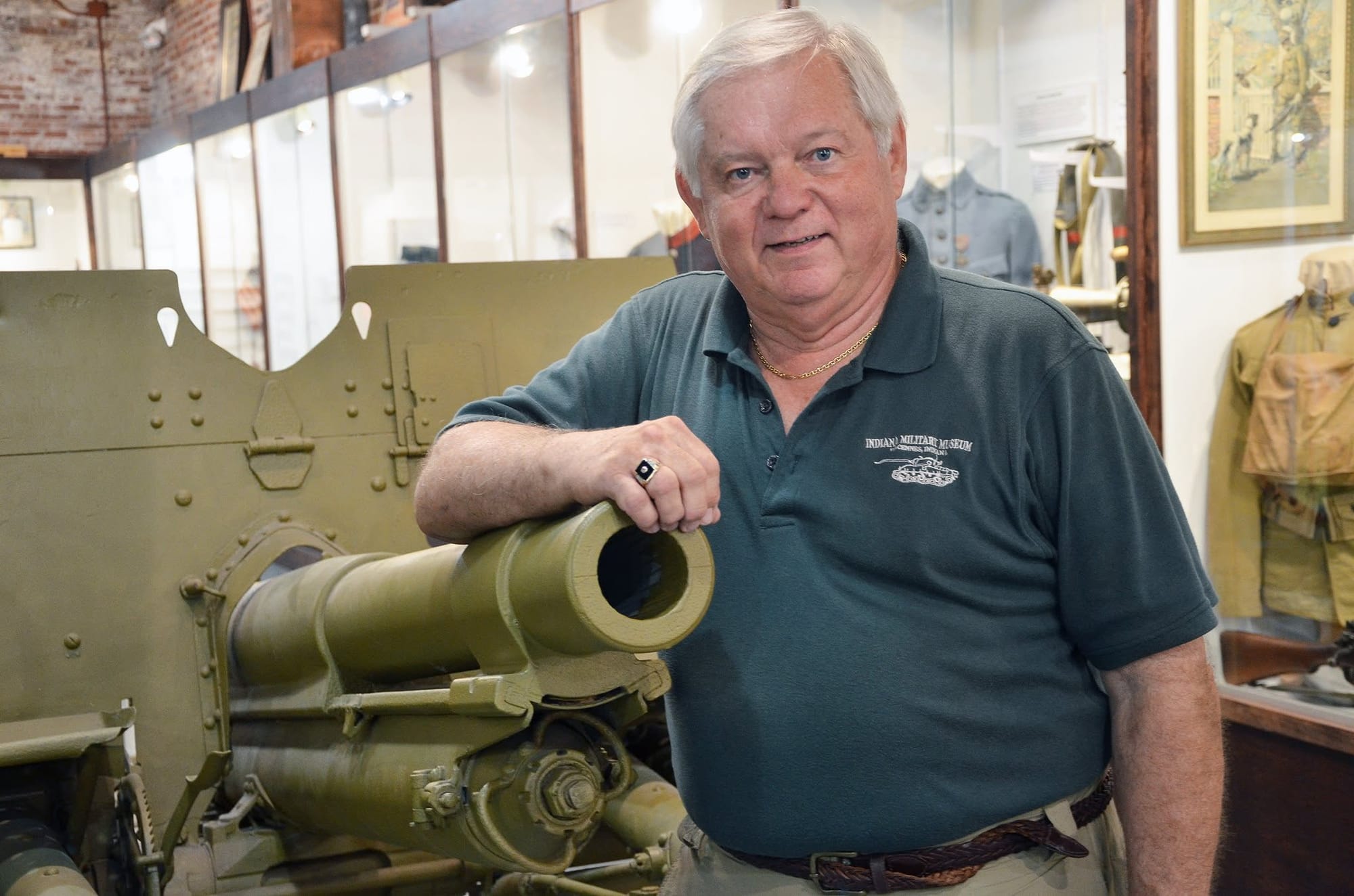 an white-haired man poses with a green American military cannon