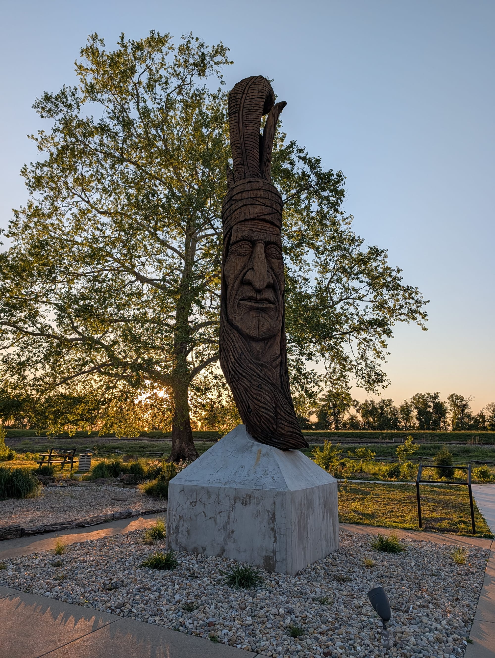a tall wooden sculpture of a deeply lined Native American man's face