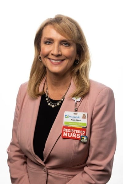 a woman wearing a pink blazer over a black shirt. Her nametag includes "REGISTERED NURSE"