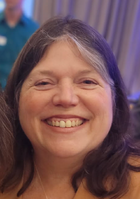 a brown-and-grey-haired woman smiles broadly at the camera in a close up of her face