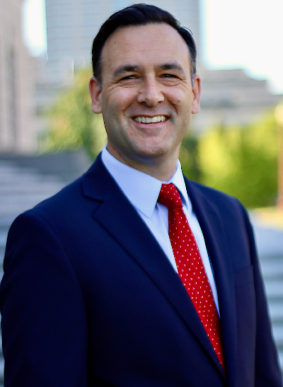 bust photo of a smiling man wearing a blue suit jacket, white shirt, and red tie