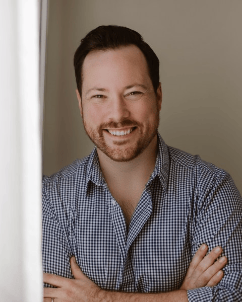 bust photo of a smiling man wearing a white and black checkered button up shirt