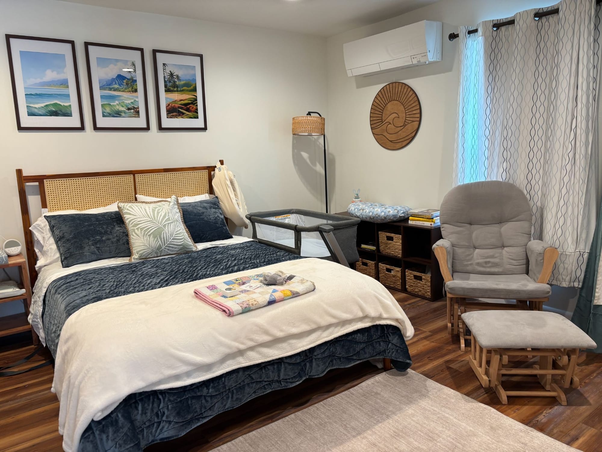 a bedroom with wall art, a rocking chair, shelving, a crib, and a large bed for mothers to rest in