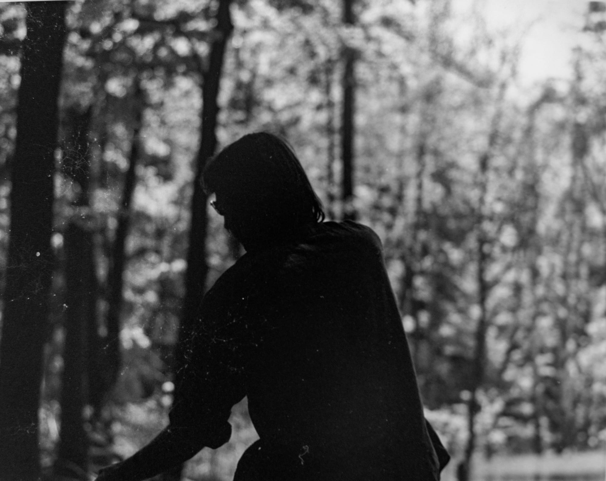 a black and white photo of a long-haired man silhouetted against trees