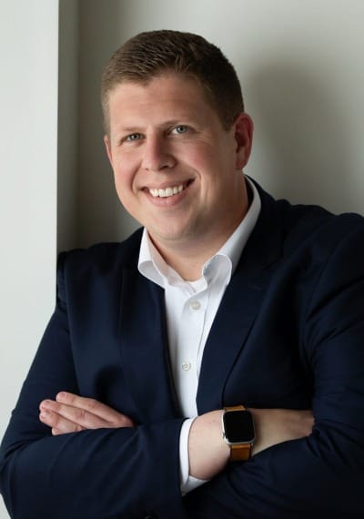 bust portrait of a blond-haired white man wearing a white button-up and a blue blazer