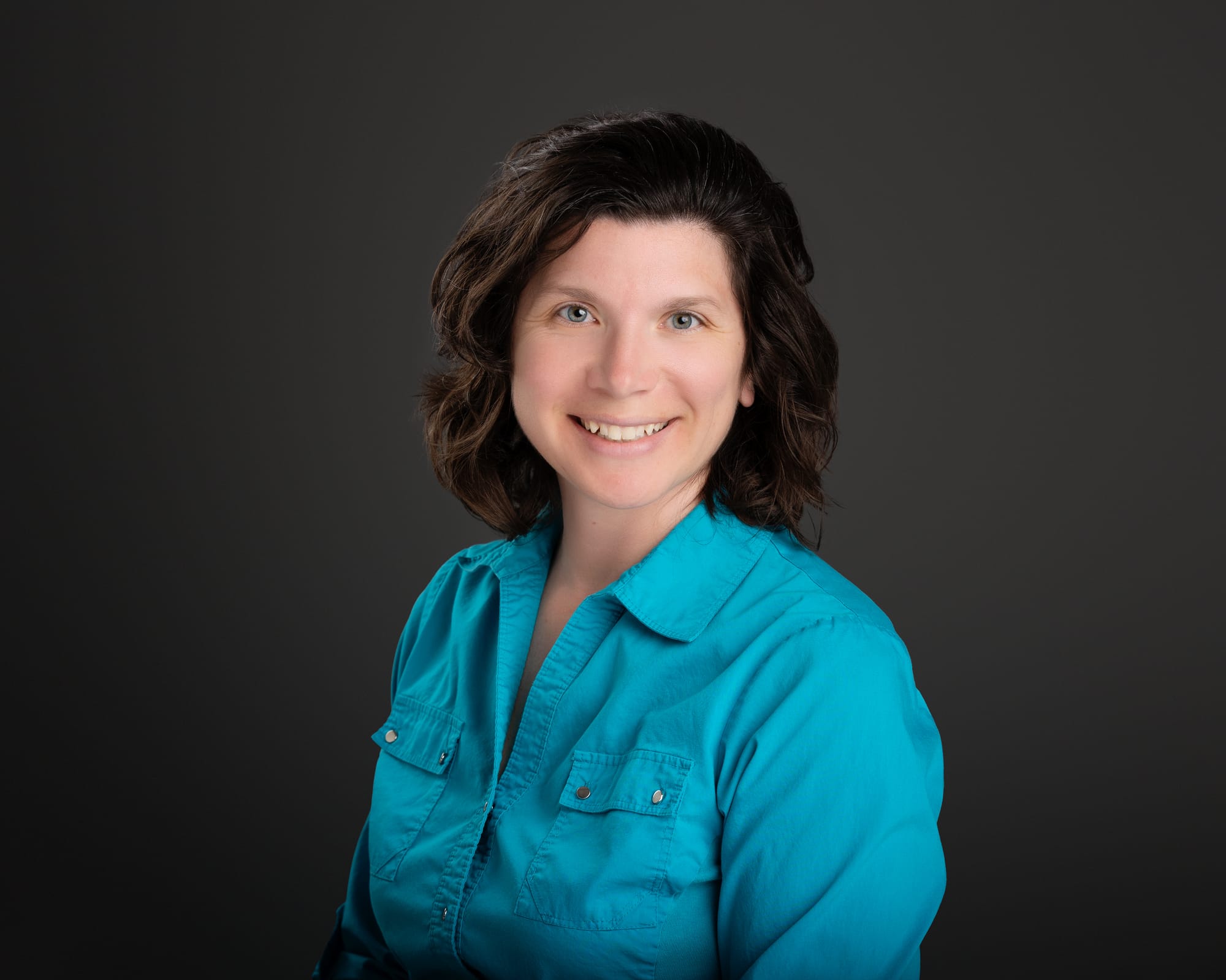 bust portrait of a brown-haired woman in a blue button down shirt