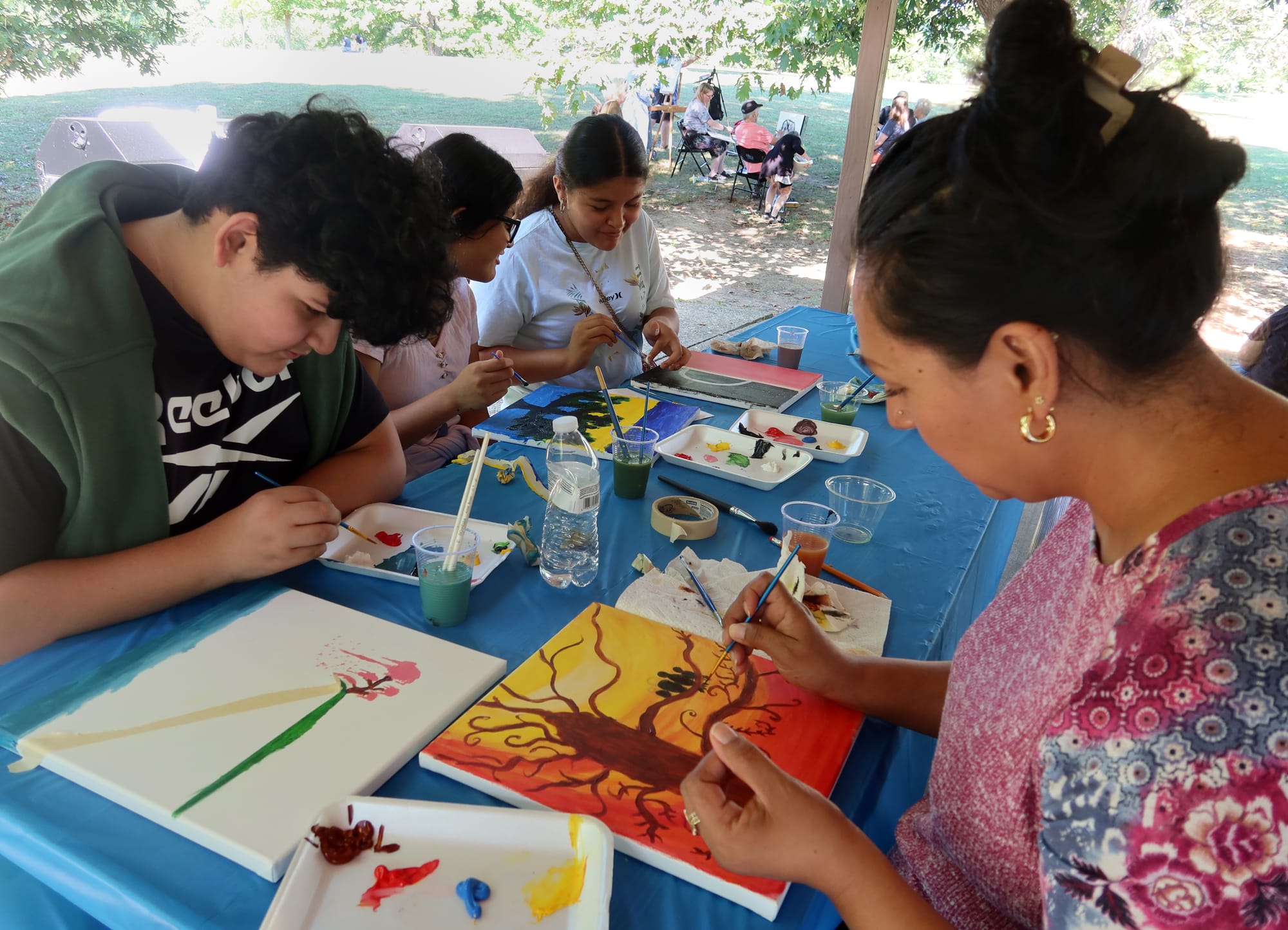 a group of young adults paint together at a picnic table