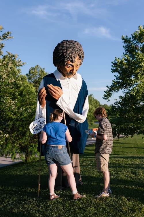 two people on a grassy knoll in a park alongside a 12-foot tall Kurt Vonnegut puppet