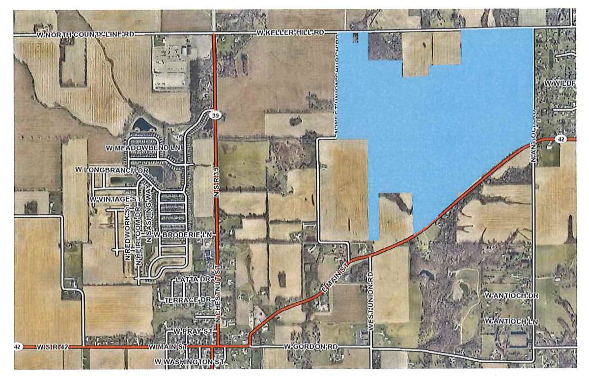 top-down aerial map showing fields, roads, and housing additions, with the proposed data center site highlighted in blue