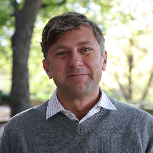 bust portrait of a man in a grey sweater over with a white striped collared shirt