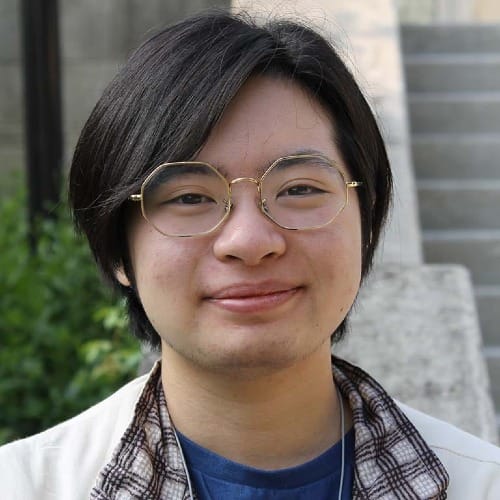 headshot of a young man wearing octagonal glasses and a white jacket