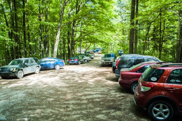 a dozen or more cars fill a gravel parking lot in the forest