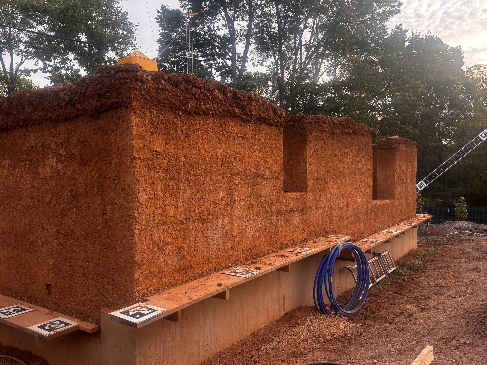 red-brown cob walls of a home-in-progress. One level of wooden scaffolding surrounds the house.