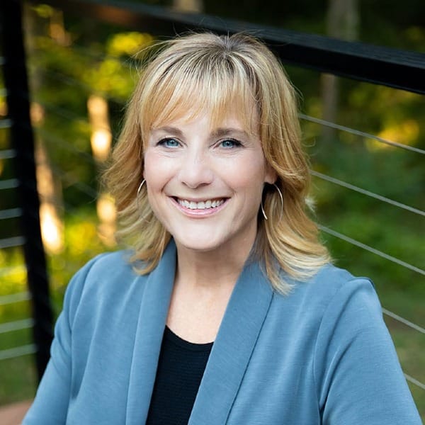 a blonde woman wearing open-hooped earrings, a black shirt, and light blue jacket