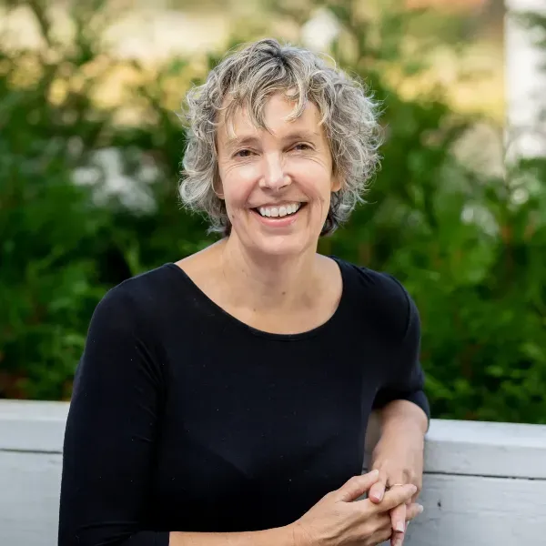 a grey-haired woman wearing a black shirt, posing with her hands together while sitting on a bench