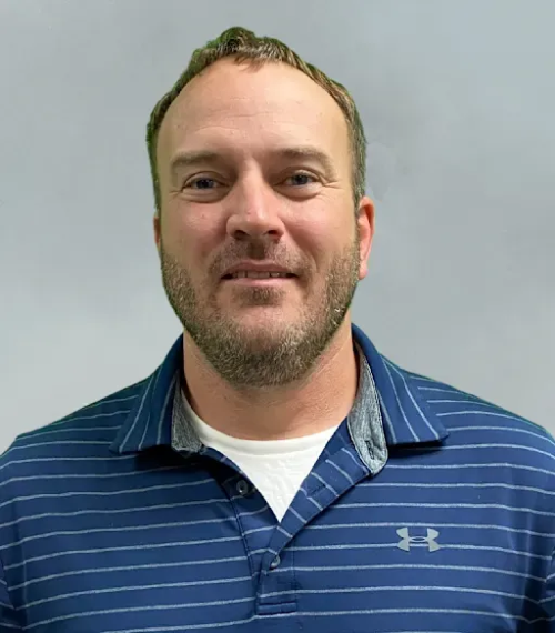 a blonde-haired man with short beard, wearing a white shirt under a blue striped Under Armour polo