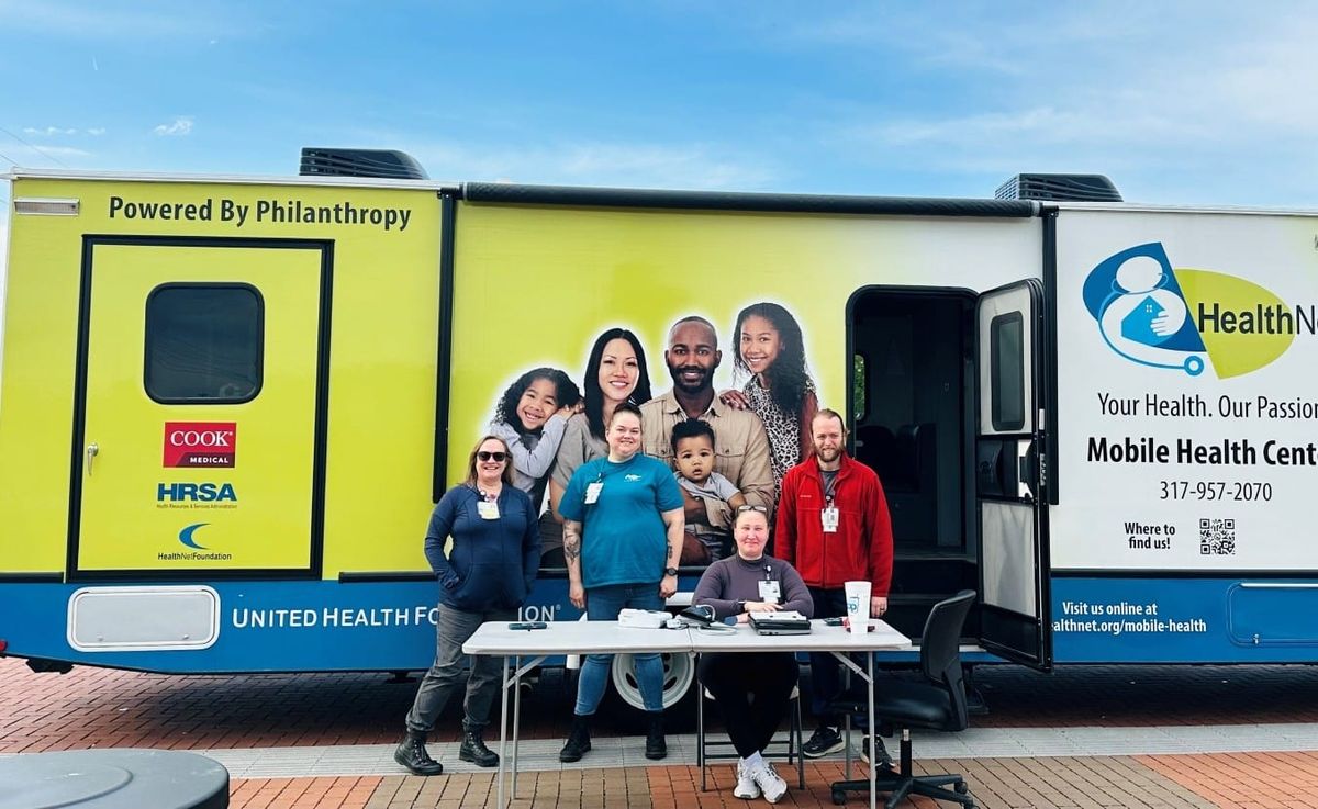 a team of healthcare professionals pose around a table in front of the RV-sized Mobile Health Center