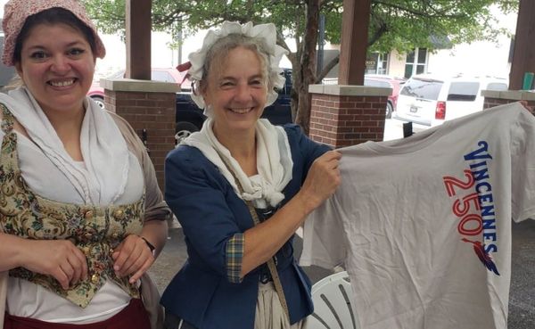 two women in replica 1700s attire display a t-shirt with the design "Vincennes 250" printed on it in blue and red