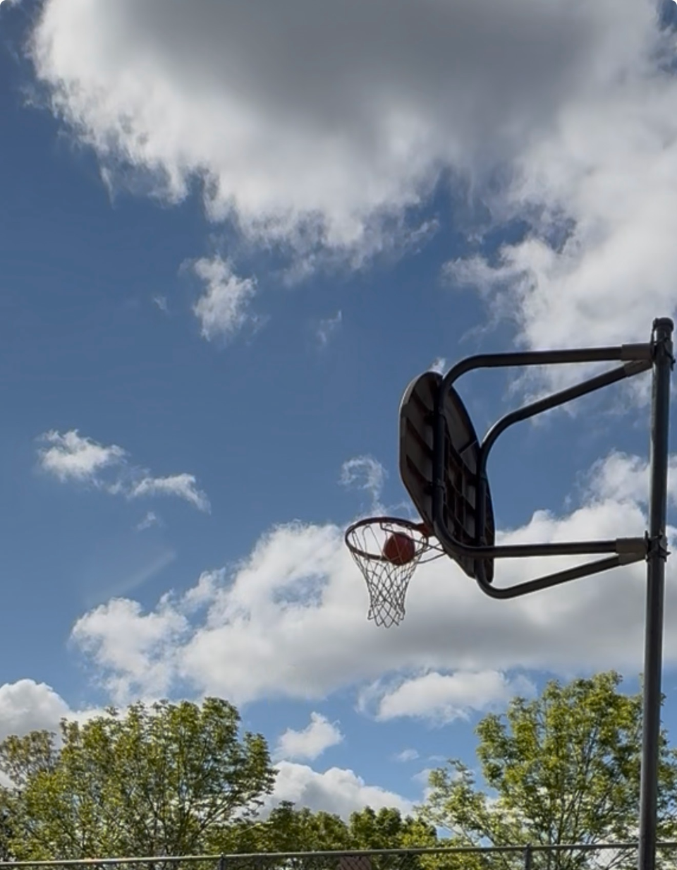 Picture of a basketball going into a net with bright blue sky as background.