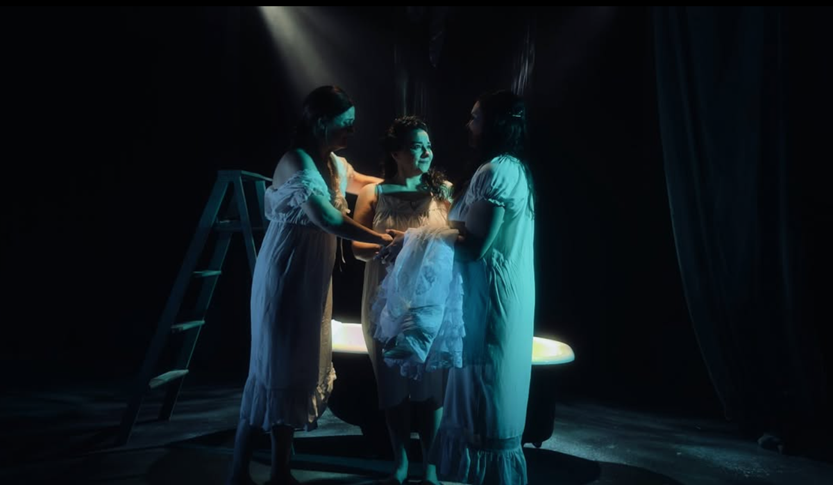 Three women in their 30s wearing nightgowns stand together.