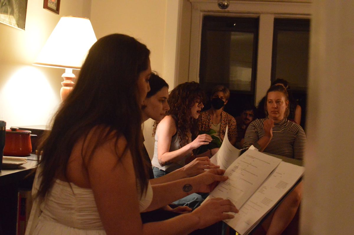 Four actors read from music stands while a few audience members look on.