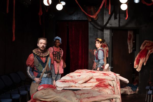 Three clowns stand surrounded by ragdolls covered in blood.