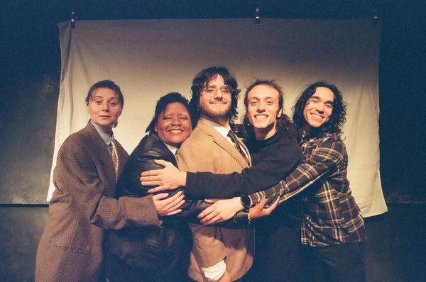 A cast of friendly faces all hug each other, wearing neutral colors.