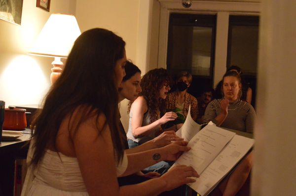 Four actors read from music stands while a few audience members look on.