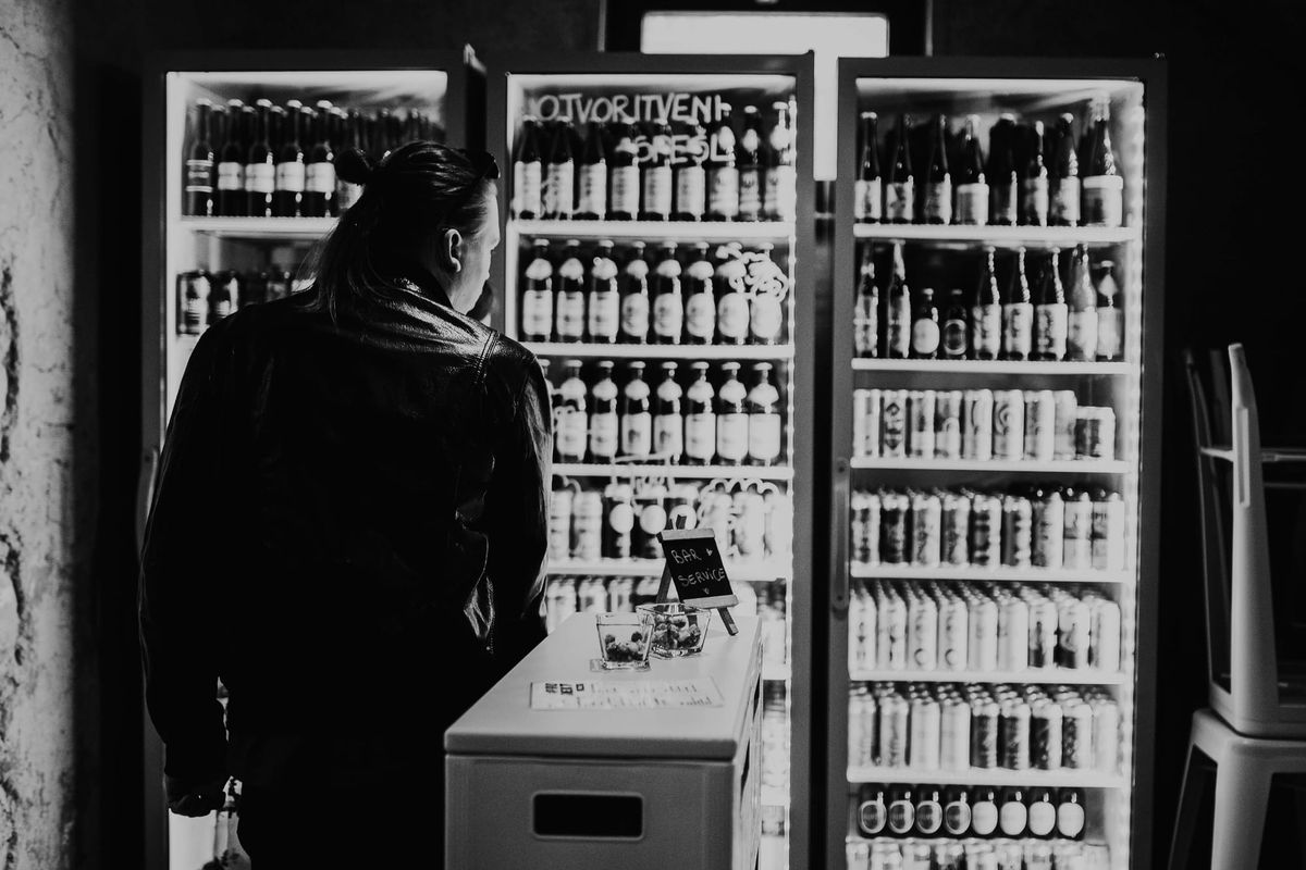 Črnobela fotografija. Ena oseba opazuje širok izbor piv v hladilniku v lokalu :Projekt.