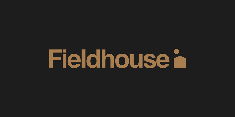 Warm color Fieldhouse logotype and logomark on a dark background. The word "fieldhouse" is set in medium bold type with a small house and sun shape to the right of it.