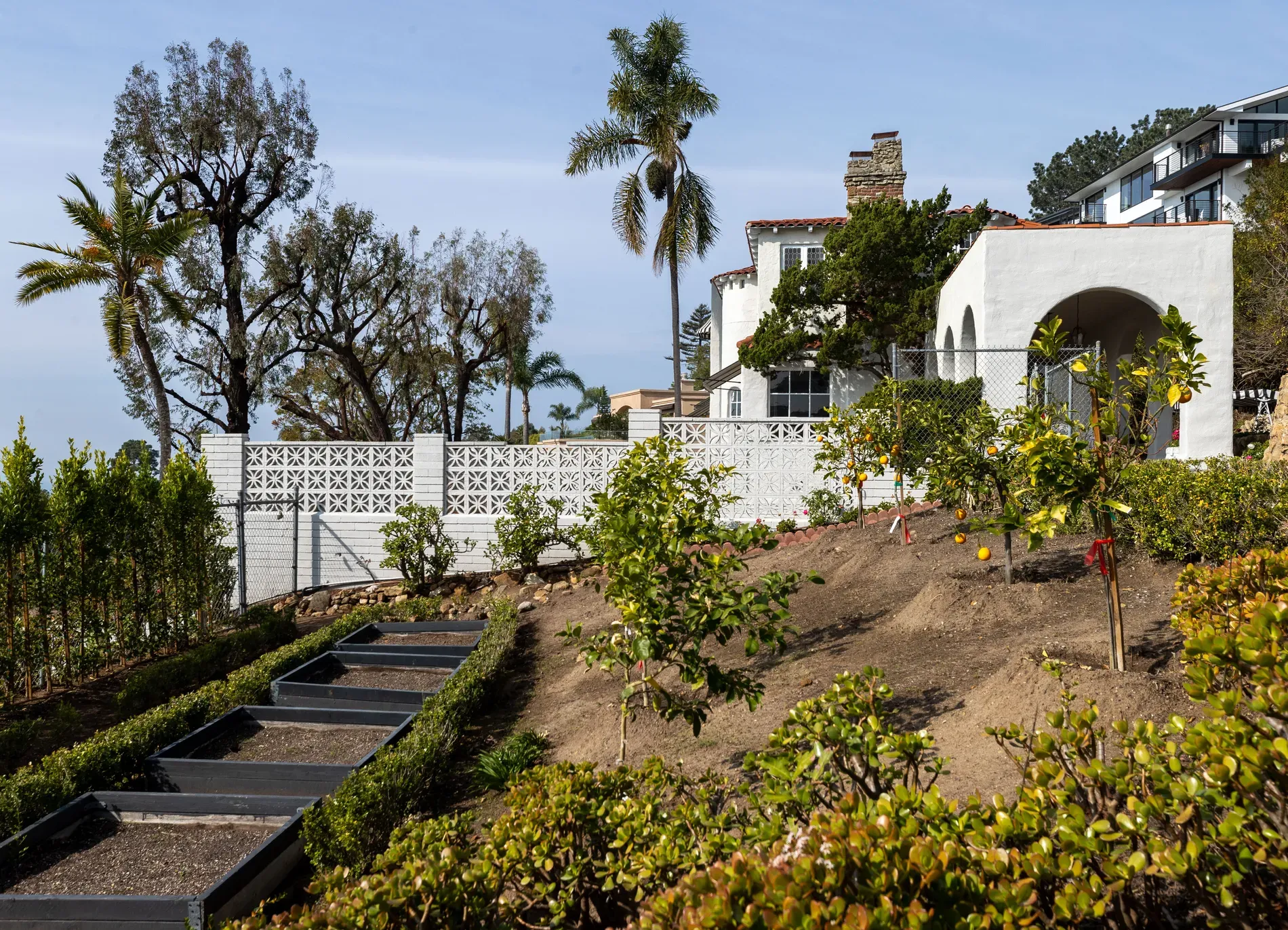 Back outside — white stucco, terra-cotta roof. Raised beds everywhere. why this layout?
