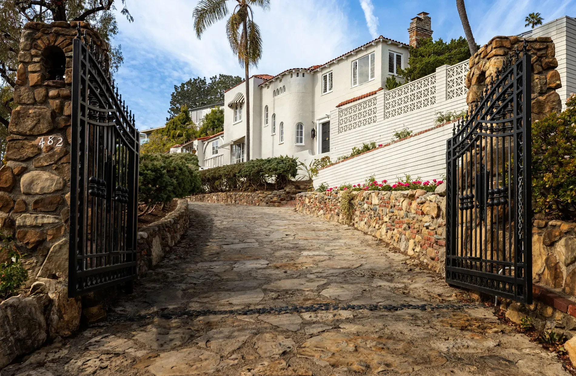 Entrance shot from above — wrought iron gates, winding stone driveway. Dramatic.