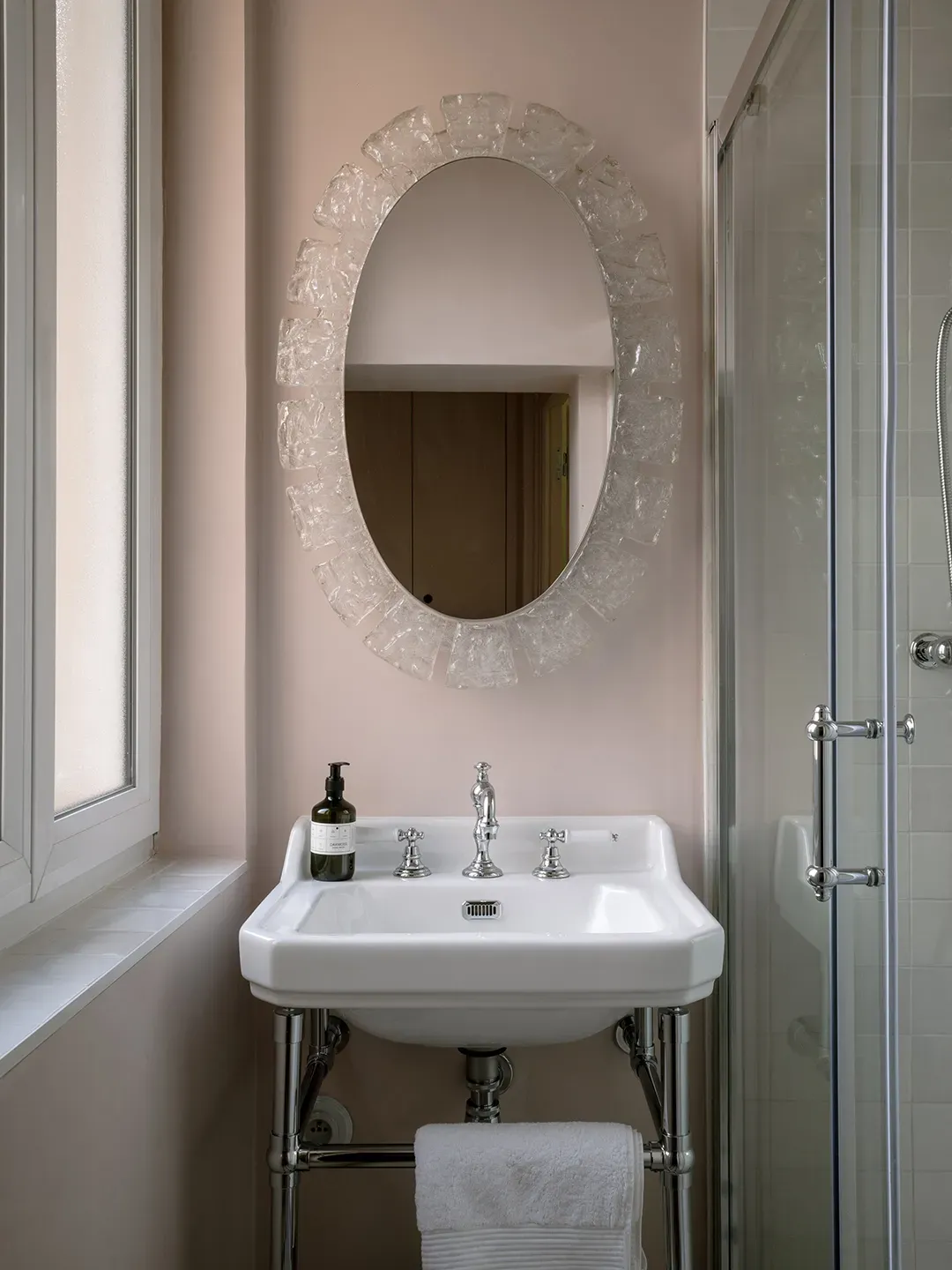 Blush bathroom with a pedestal sink — that frosted oval mirror kinda slaps.