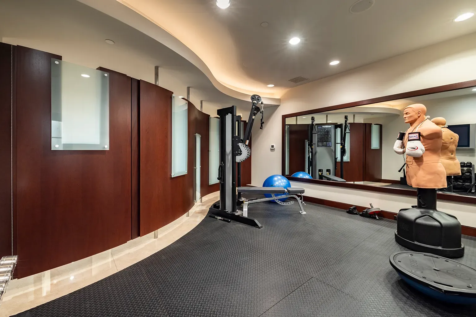 Gym with curved mahogany walls. Fancy sweat zone. Mirror makes it feel huge.