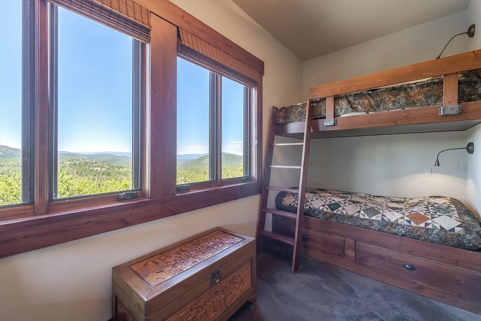 Bunk room that doesn’t feel cramped. Dark wood, patterned quilt, daylight doing overtime.