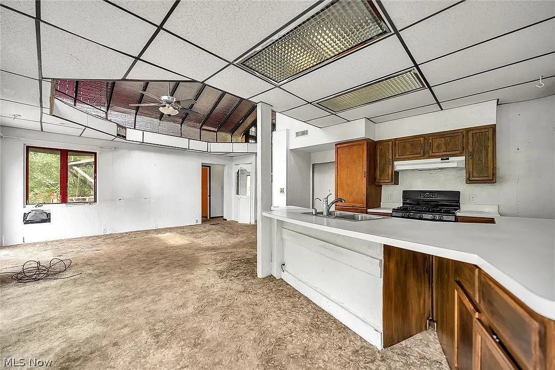 Open living room into kitchen, beige carpet, bar-height counter ready for stools.