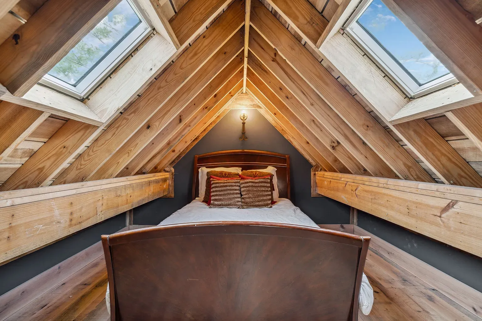 A-frame attic bedroom. Moody wall, warm wood, feels a quiet treehouse.