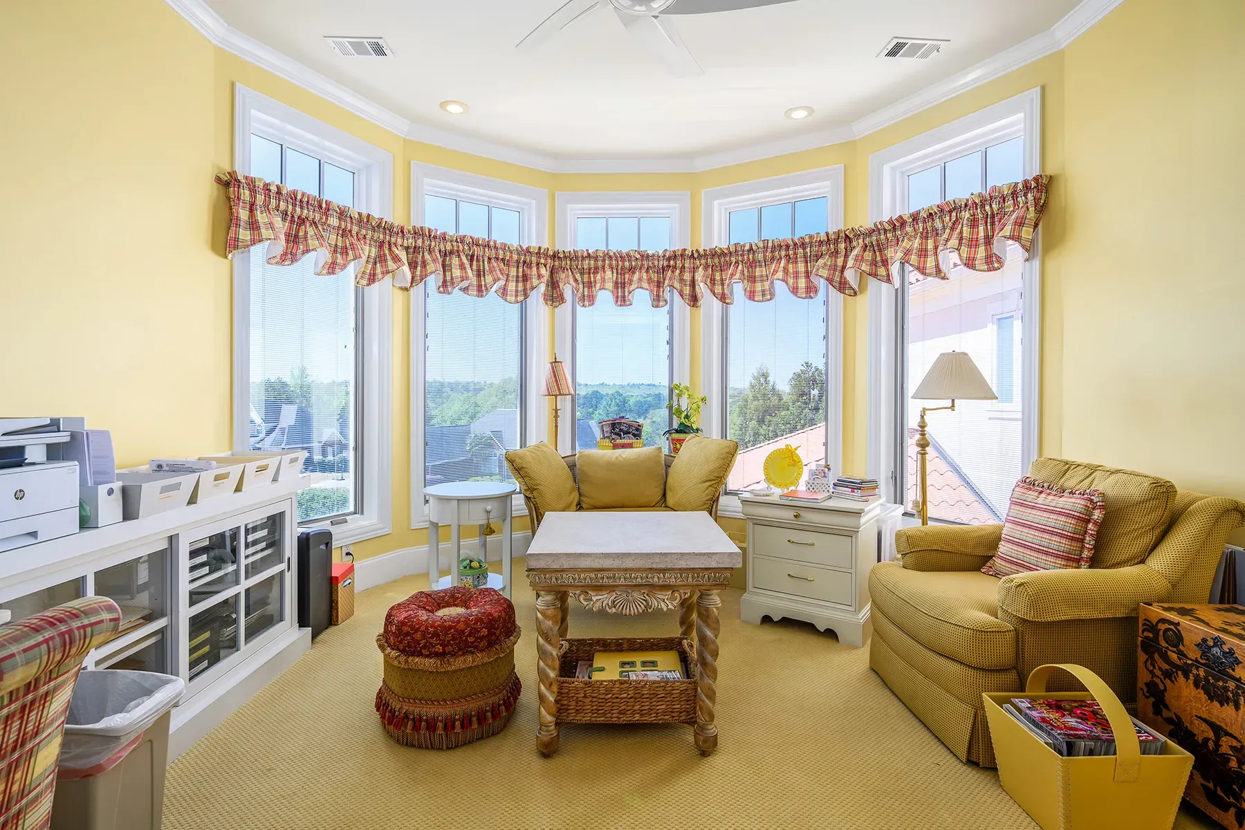 Sunroom is cheerful—soft yellow, plaid valance, plants soaking up light.
