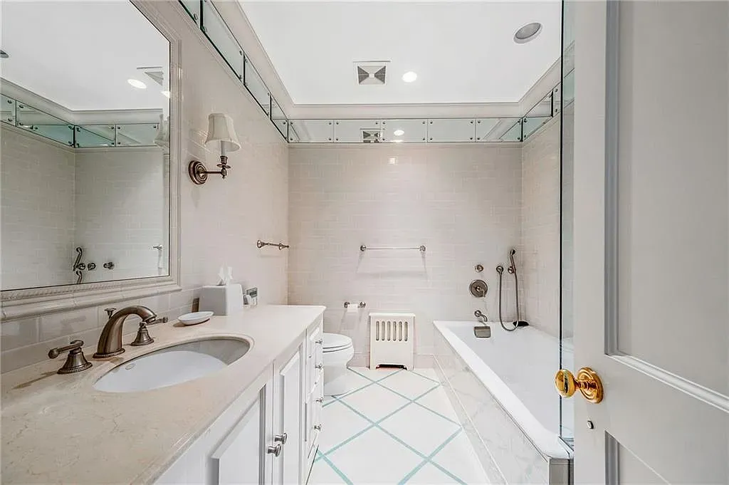Bathroom is pale and serene. Glass shower keeps it airy.