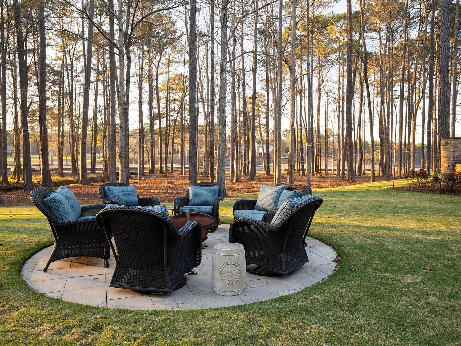 An outdoor fire pit area with black chairs surrounded by tall trees