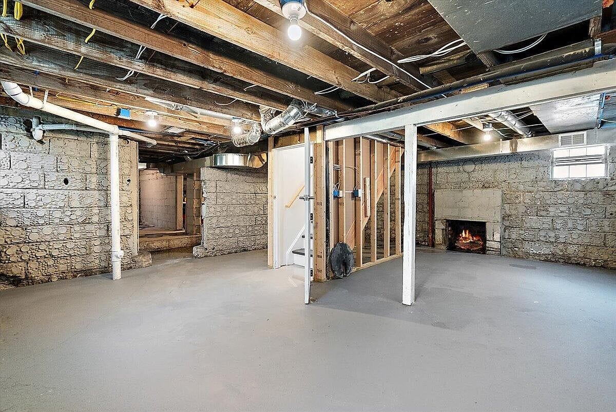 Unfinished basement showing stone walls and a fireplace