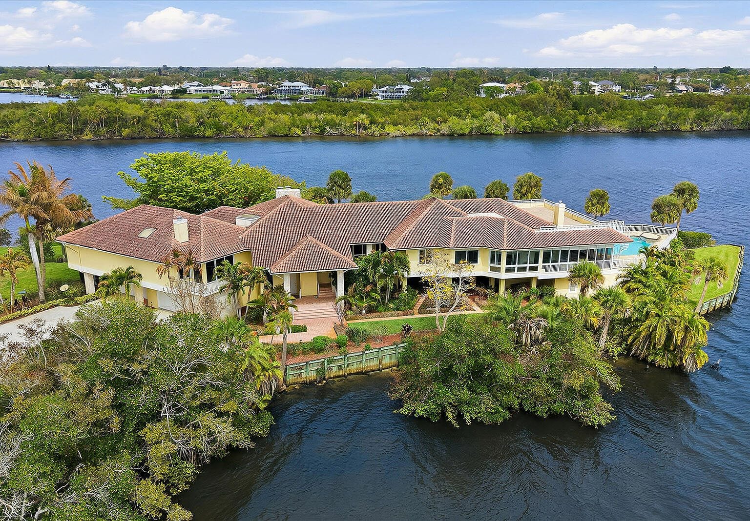 Drone view showing the massive yellow house sitting on a private peninsula surrounded by blue water