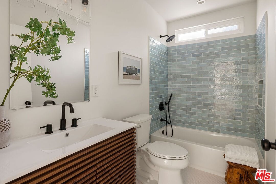 Bathroom featuring blue-grey subway tiles in the tub and a wood slat vanity