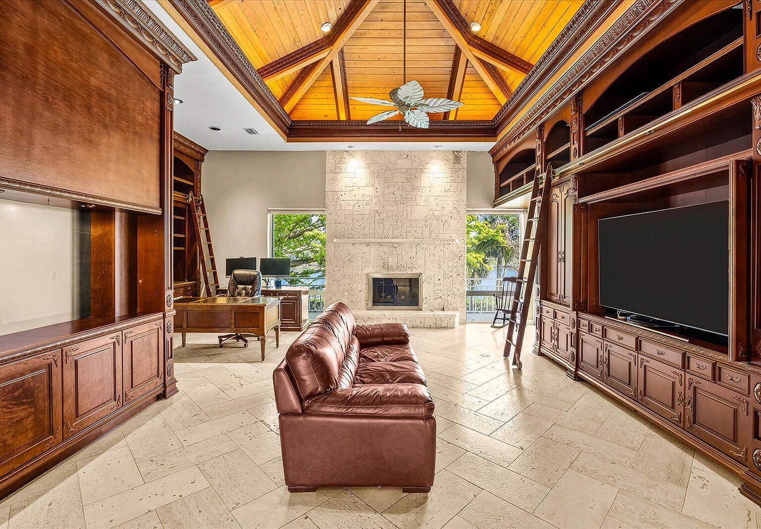 Two-story library with dark wood bookshelves, a ladder, and a stone fireplace