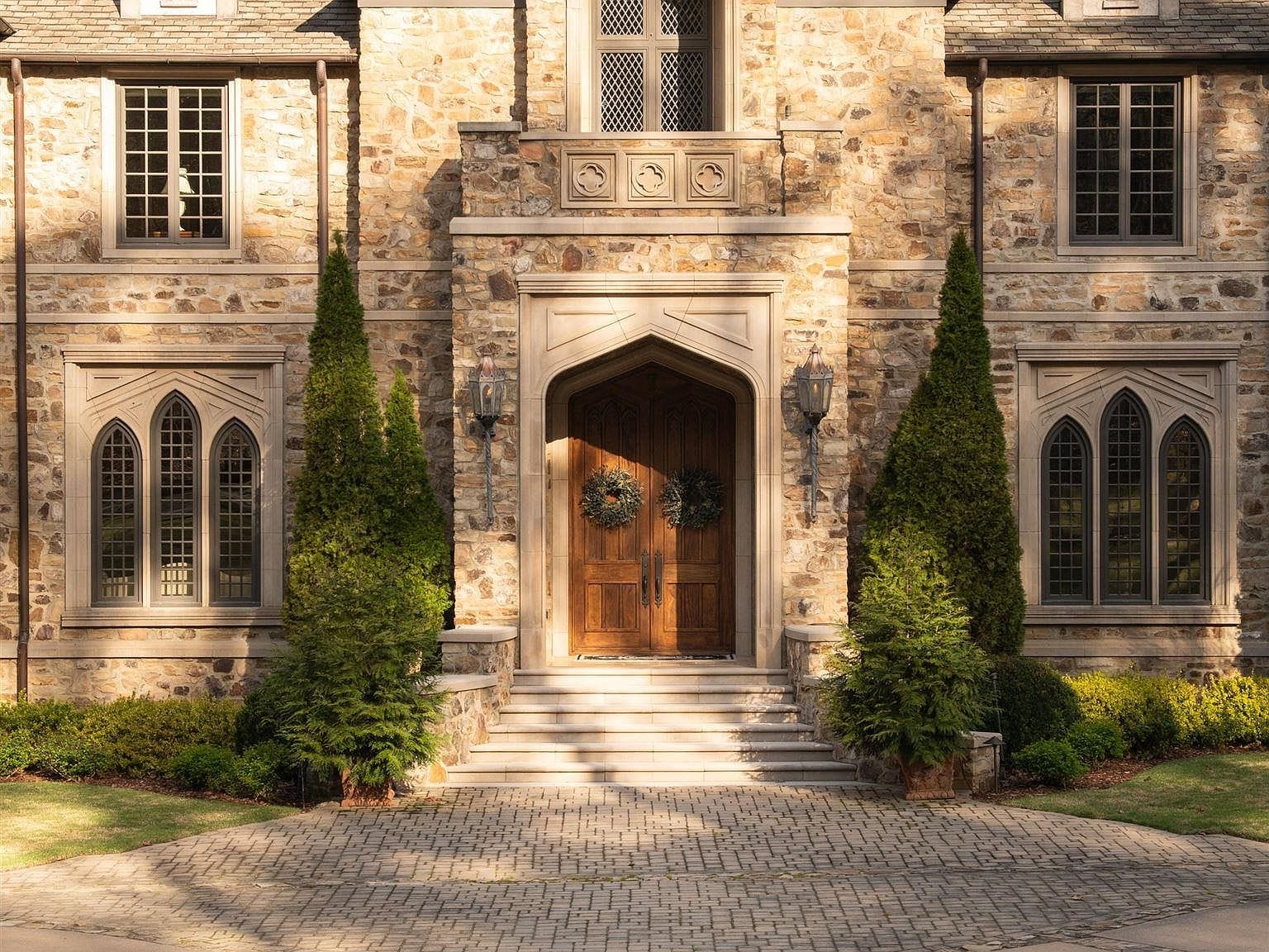 The arched wooden front door surrounded by stone and tall pine trees