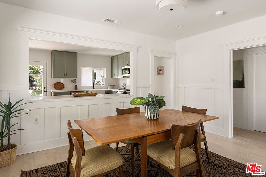 Wooden dining table with a view through the wall cutout into the kitchen